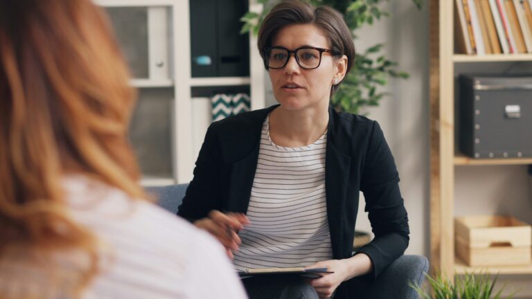 A clinician holding a clipboard during a one-on-one consultation in an office.
