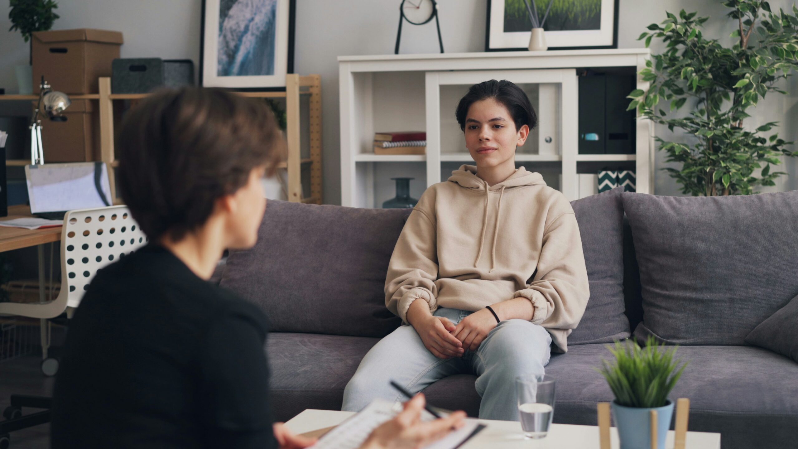 A young client talking with a counselor who is taking notes in a therapy office.