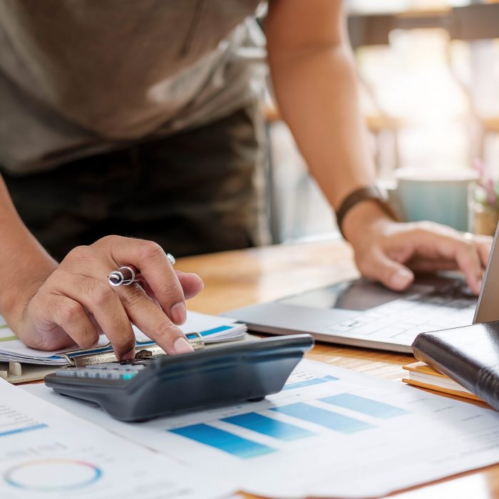 Close up of businessman or accountant hand holding pen working on calculator to calculate business data, accountancy document and laptop computer at office, business concept