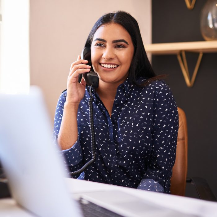 Young indian businesswoman talking on a telephone in an office alone. One female only making a call while working as a receptionist at a front desk. Administrator and secretary consulting and transferring calls from a help desk in a call centre
