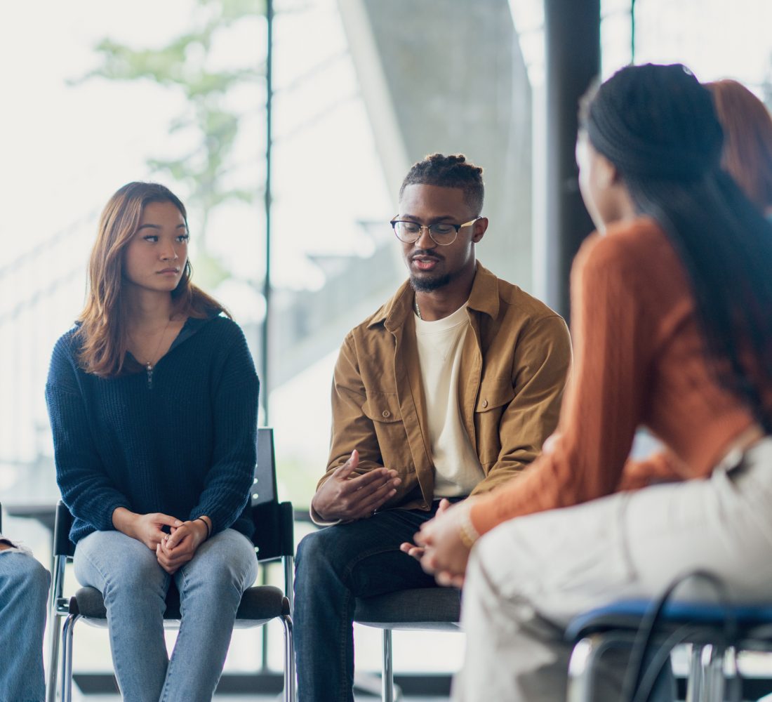 A small group of University students sit together during a group therapy session.  They are each dressed casually as they take turns sharing their struggles with the group.