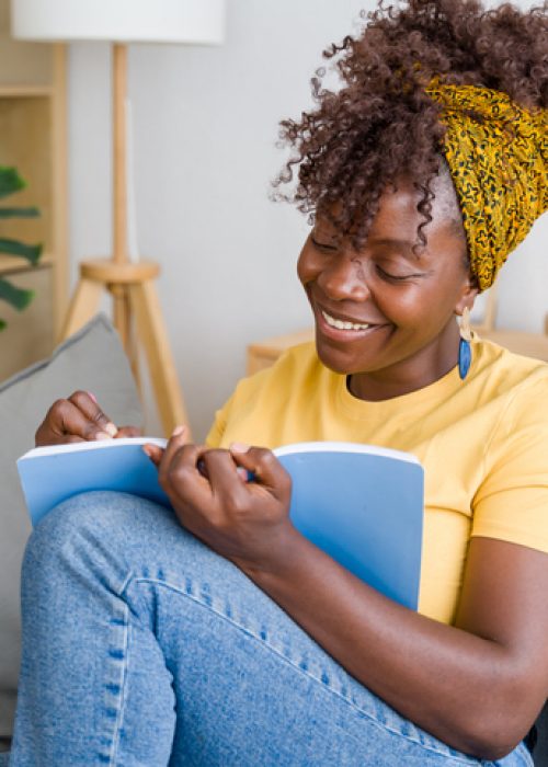 Young woman is smiling while writing in her notebook, enjoying her free time at home