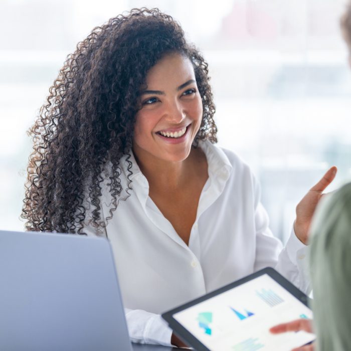 Business man and business woman in a meeting at the office. There is a laptop on the table and the man is holding a digital tablet with finance chart and graphs. They are both smiling and happy