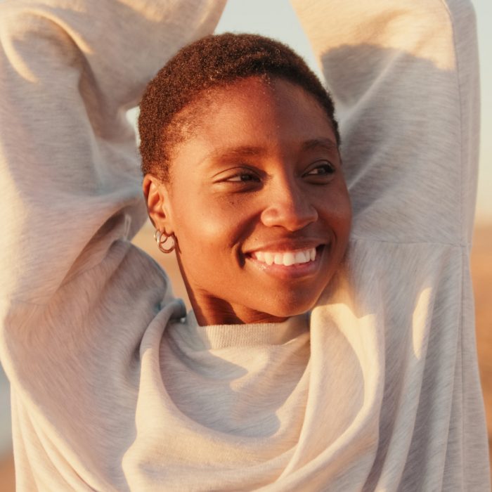 A girl smiles and raises her arms to the sky at dawn on the beach