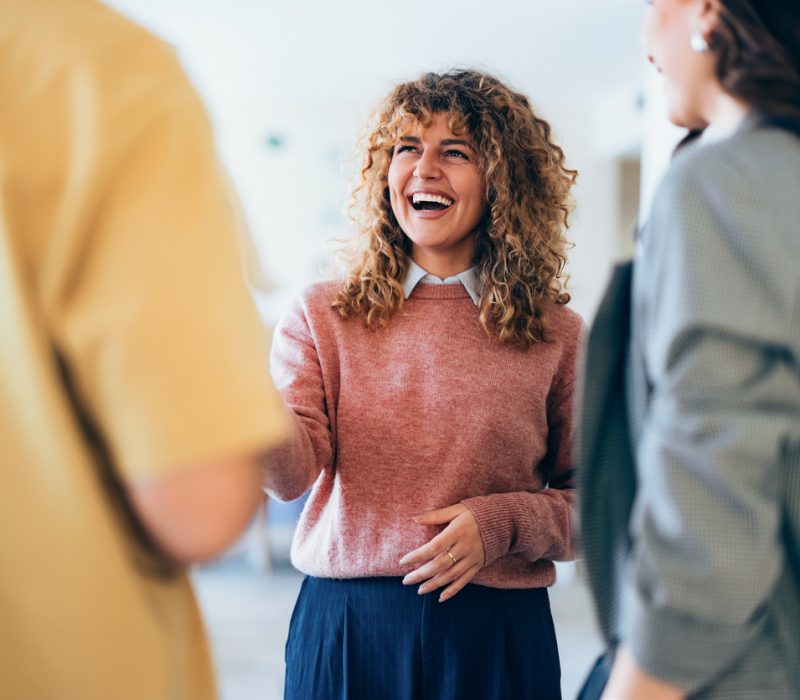 Smiling individuals interact and enjoy casual conversation in a welcoming professional atmosphere, promoting positivity and collaboration.