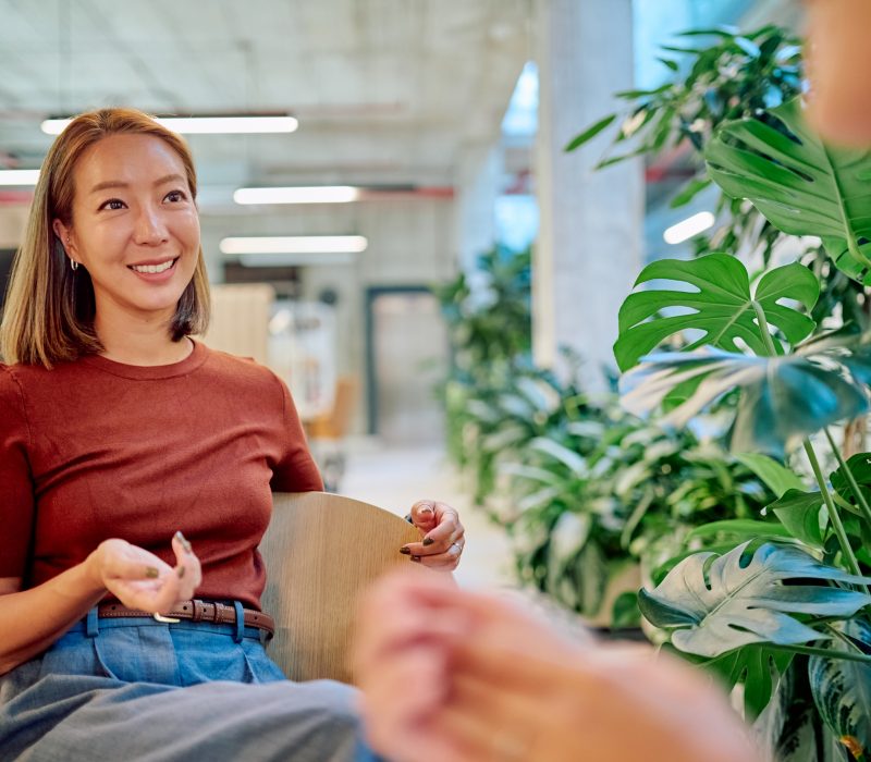Asian businesswoman gesturing while discussing with colleague in a modern green office with many plants